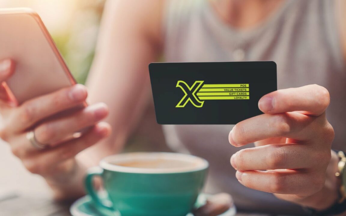 Woman enjoying a coffee while holding a Givex gift card and cell phone