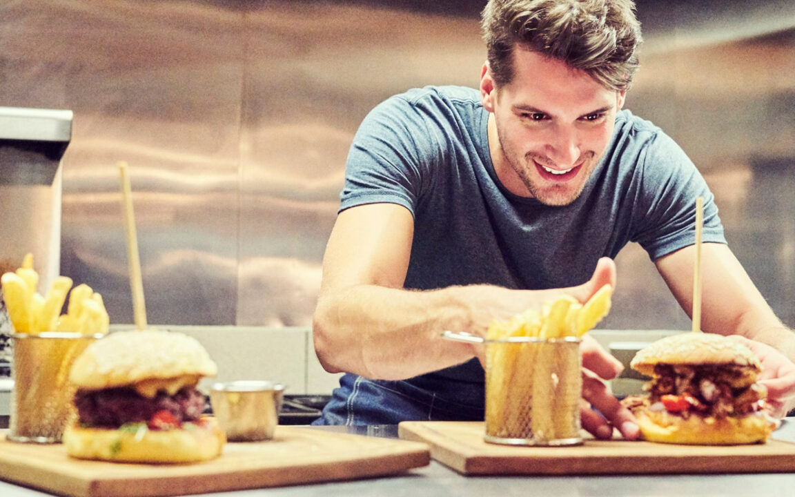 Happy-chef-arranging-burger-and-French-fries-641732094_1900x770px
